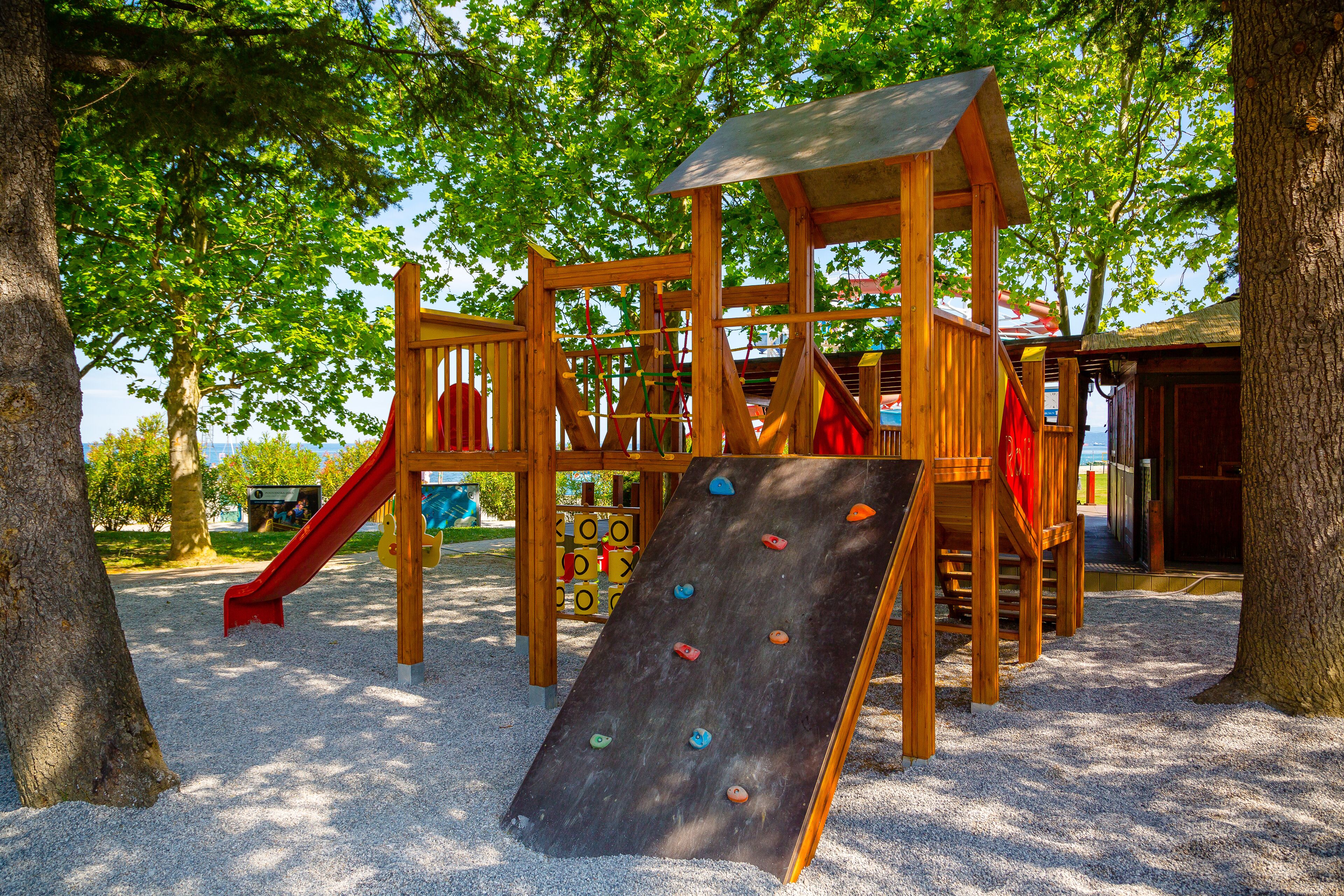 Ein Spielplatz mit Klettergerüsten und einer Rutsche, umgeben von Bäumen und sandigem Untergrund.