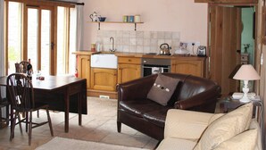 A cozy living room with a leather sofa and a dining table with chairs. A kitchen with wooden cabinets and a tiled backsplash is visible in the background. - 3 bedroom accommodation in Llangwm, near Usk (Llangwm, near Usk)