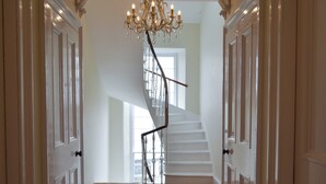 Eine prachtvolle Treppe mit einem Chandelier, Holzboden und einem roten Teppich mit Muster.