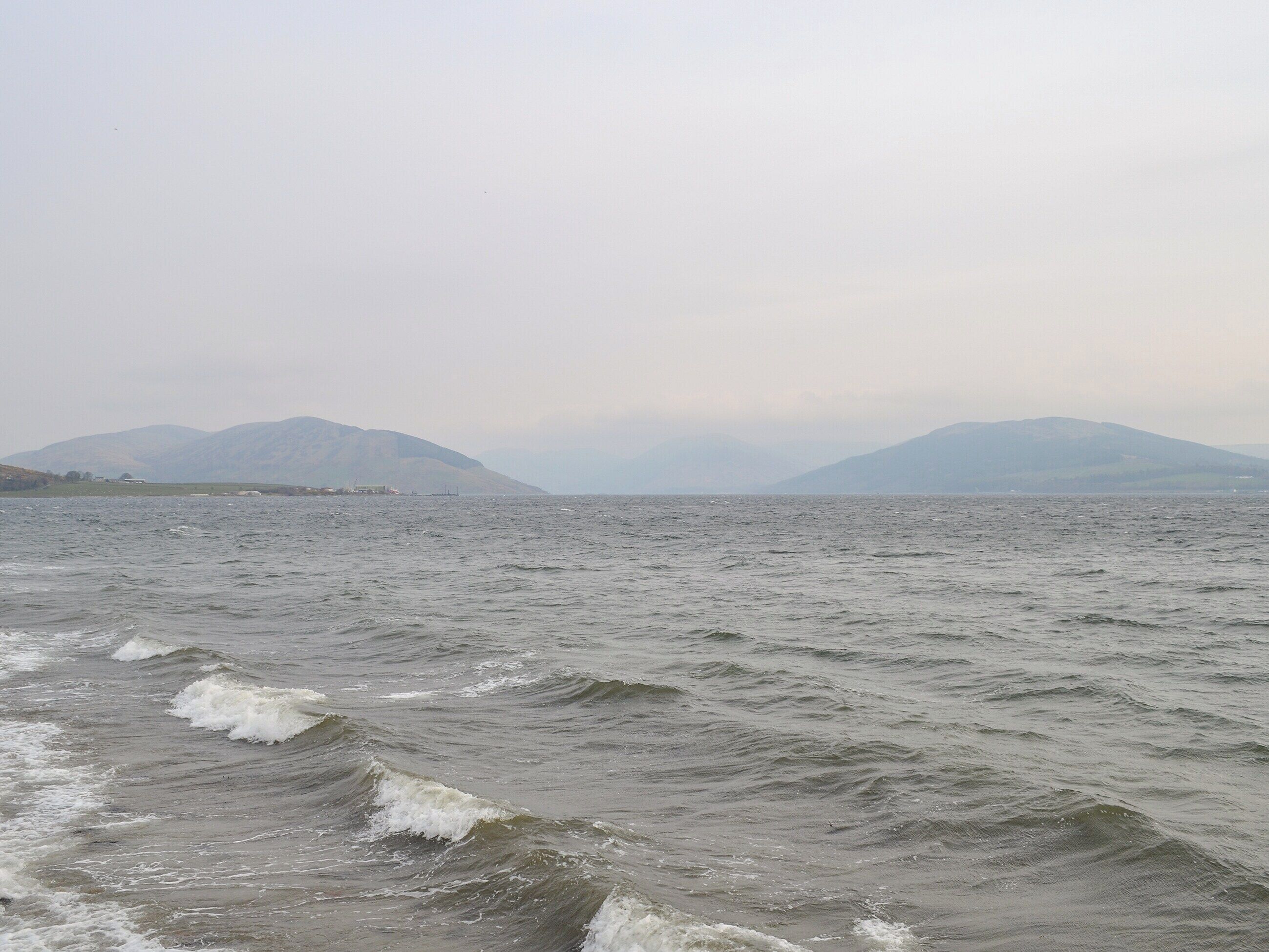 A view of a body of water with waves, distant mountains, and a hazy sky.