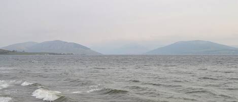 A view of a body of water with waves, distant mountains, and a hazy sky.