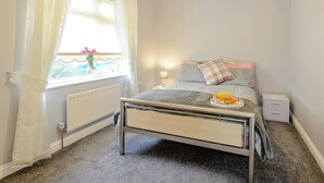 A bedroom with a bed, a radiator, a window with curtains, a bedside table with a lamp, and a tray with breakfast items. - 1 bedroom accommodation in Cawston, near Aylsham (Cawston, near Aylsham)