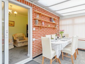 A dining area with a brick wall, wooden shelves, and a table set for two. - 1 bedroom accommodation in Cawston, near Aylsham (Cawston, near Aylsham)