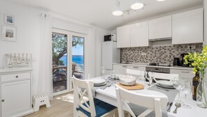 Une cuisine moderne avec des meubles blancs, un pare-feu en carreaux et une vue sur la mer par une porte vitrée.