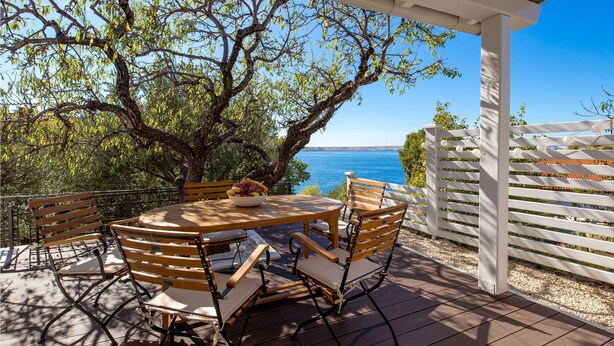 Une terrasse extérieure avec une table et des chaises en bois rondes, une pergola blanche et une vue sur la mer.