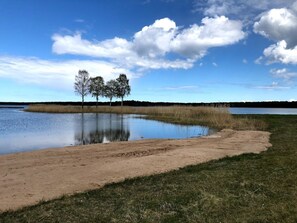 A lakeside view with a sandy beach, grassy area, and trees in the background. - Pensionat Grankullavik (Byxelkrok)