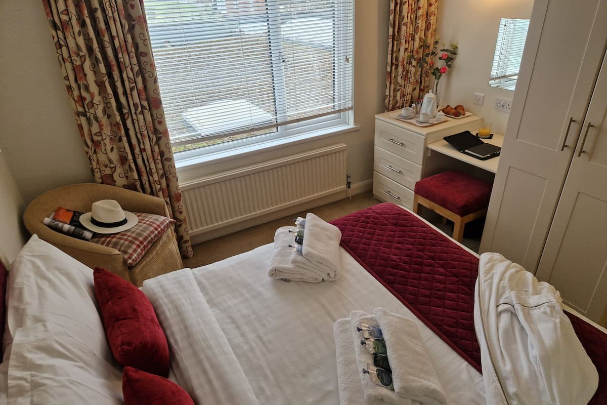 A hotel room with two beds, a desk, a chair, a radiator, and a window with curtains.