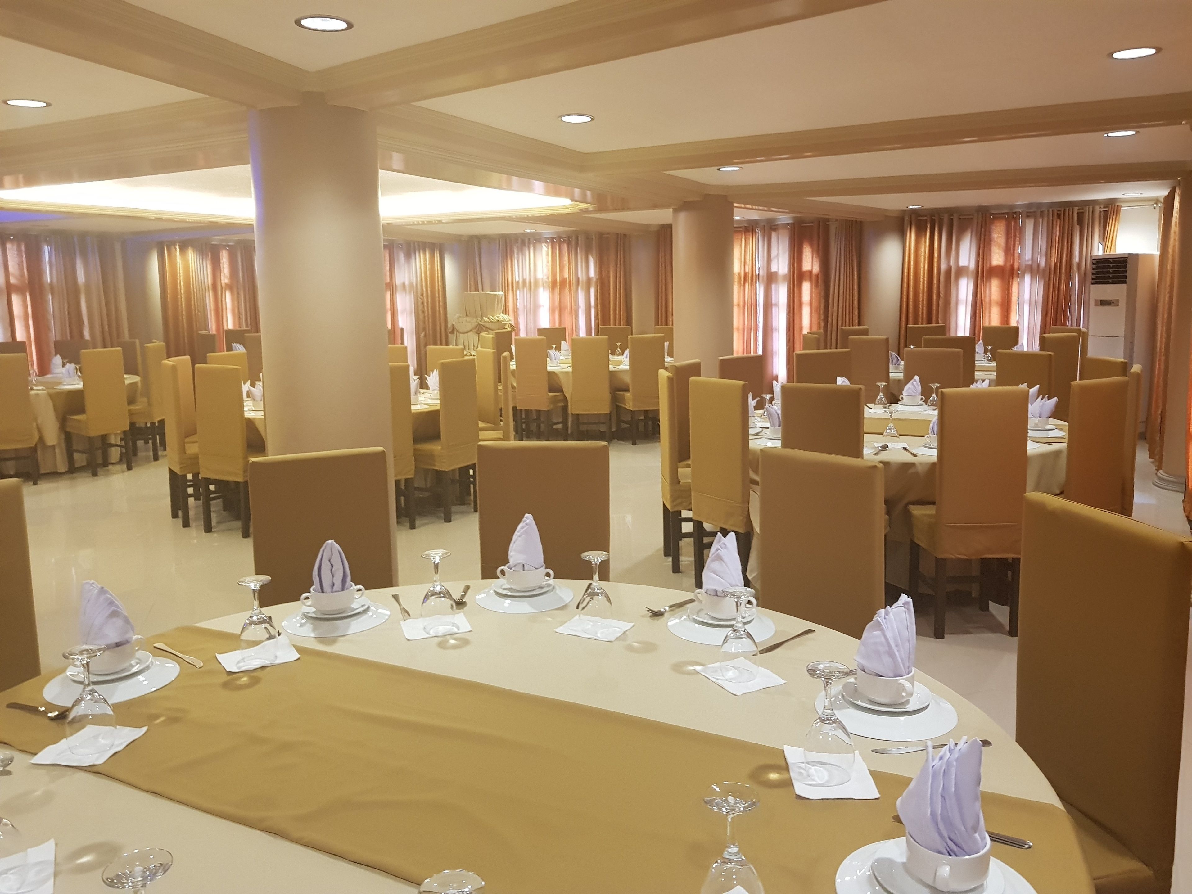 A hotel dining area with multiple tables set for dining, each with white tablecloths, silverware, and wine glasses.
