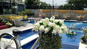 A pool area with a bicycle adorned with flowers, surrounded by greenery and a dining setup. - Villa Esmeralda Bryan's Resort Hotel and Restaurant (Palayan City)