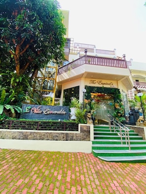 A hotel entrance with a sign reading 'The Esquivel's Lovvy,' a staircase, and a lush garden area.
