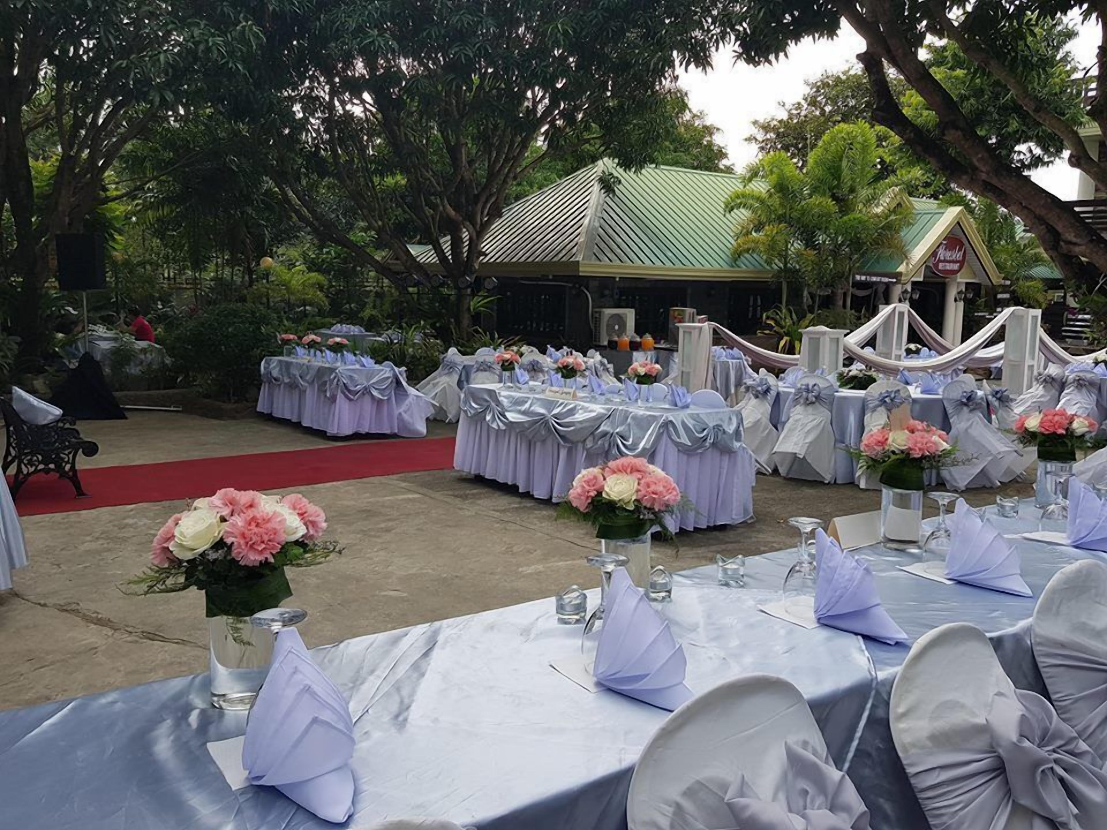 Un espacio para eventos al aire libre con mesas redondas cubiertas con manteles blancos y servilletas azules, dispuestas en filas y con centros de mesa florales.