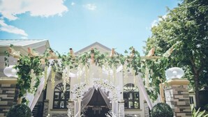 A wedding arch with white flowers and greenery, set against a building with a stone facade and arched windows. - Villa Esmeralda Bryan's Resort Hotel and Restaurant (Palayan City)