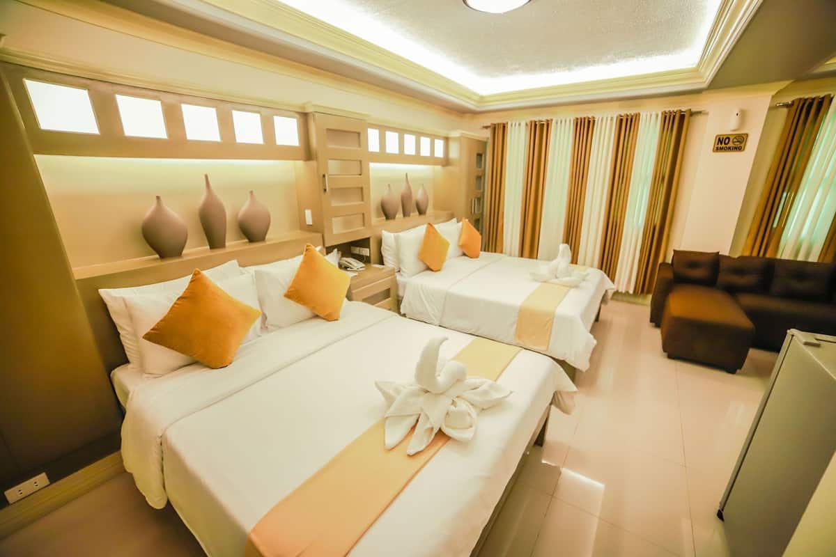A hotel room with two beds, a sofa, a TV, and a 'No Smoking' sign.