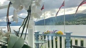 A potted orchid on a windowsill with a view of a balcony, flags, and a distant landscape. - Eidsvåg Fjordhotell (Molde)
