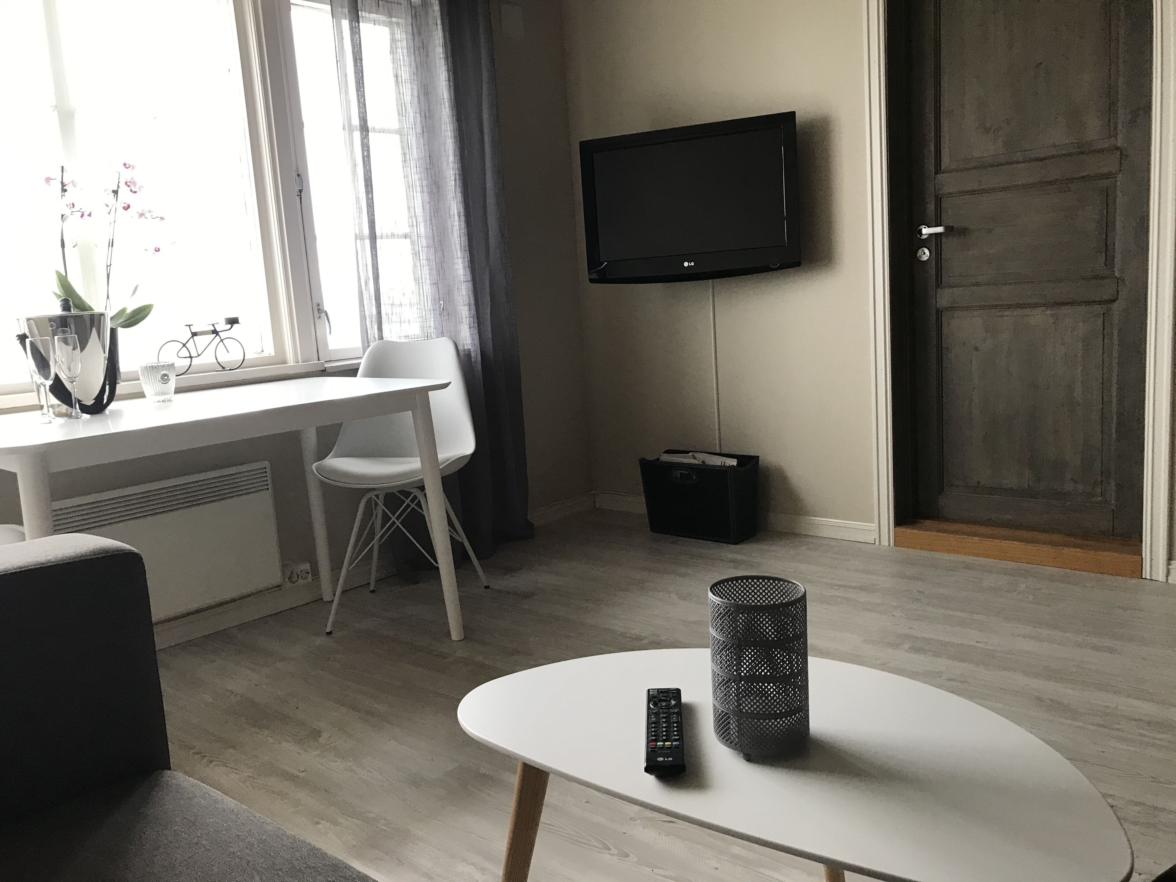 A modern living room with a white table, a white chair, a TV mounted on the wall, and a door.