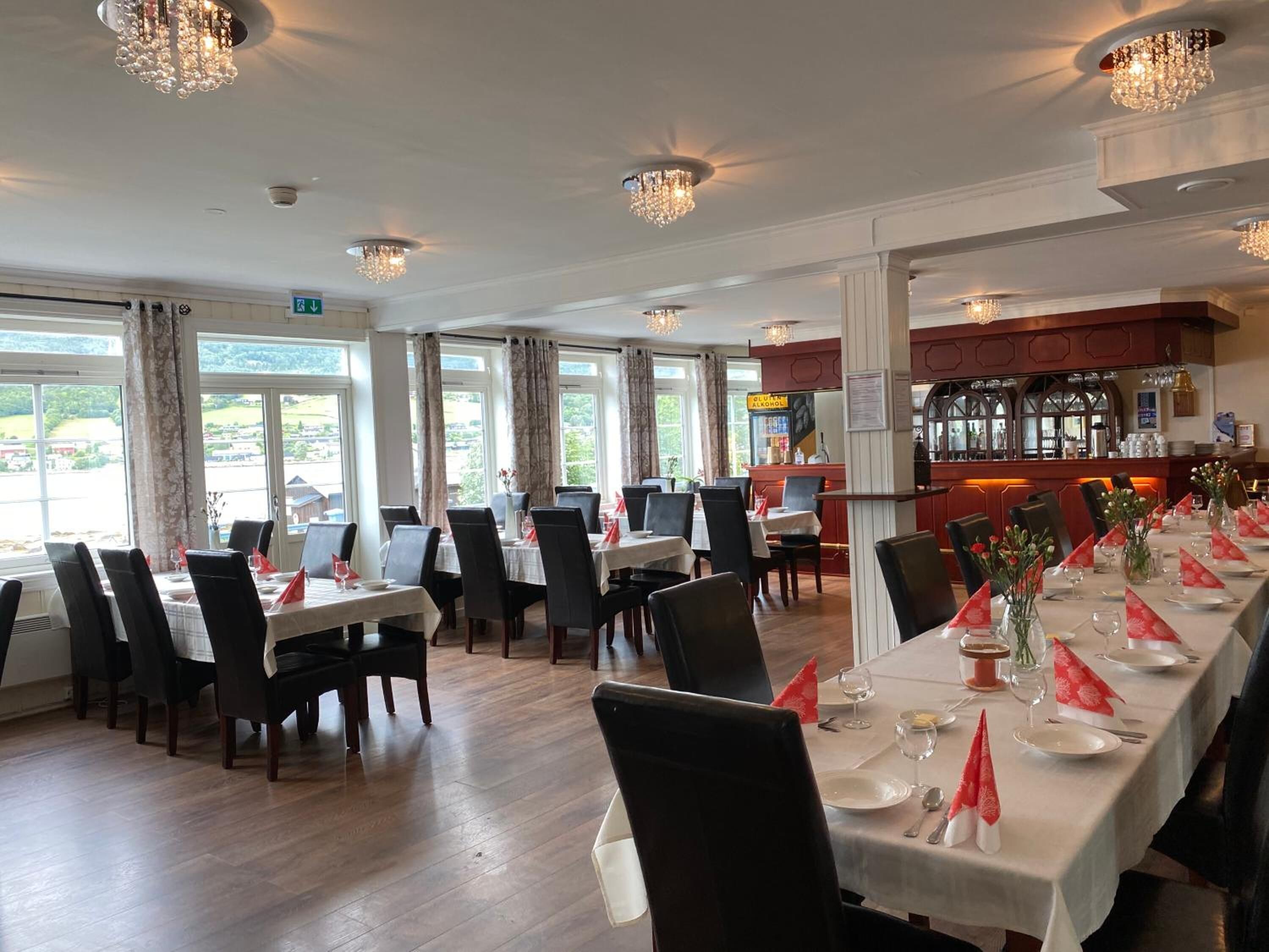 A restaurant with multiple tables set for dining, large windows, and a bar area.