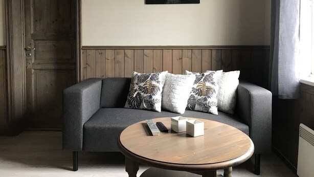 A room with a grey sofa, a round wooden coffee table, and a painting of a landscape on the wall. - Eidsvåg Fjordhotell (Molde)