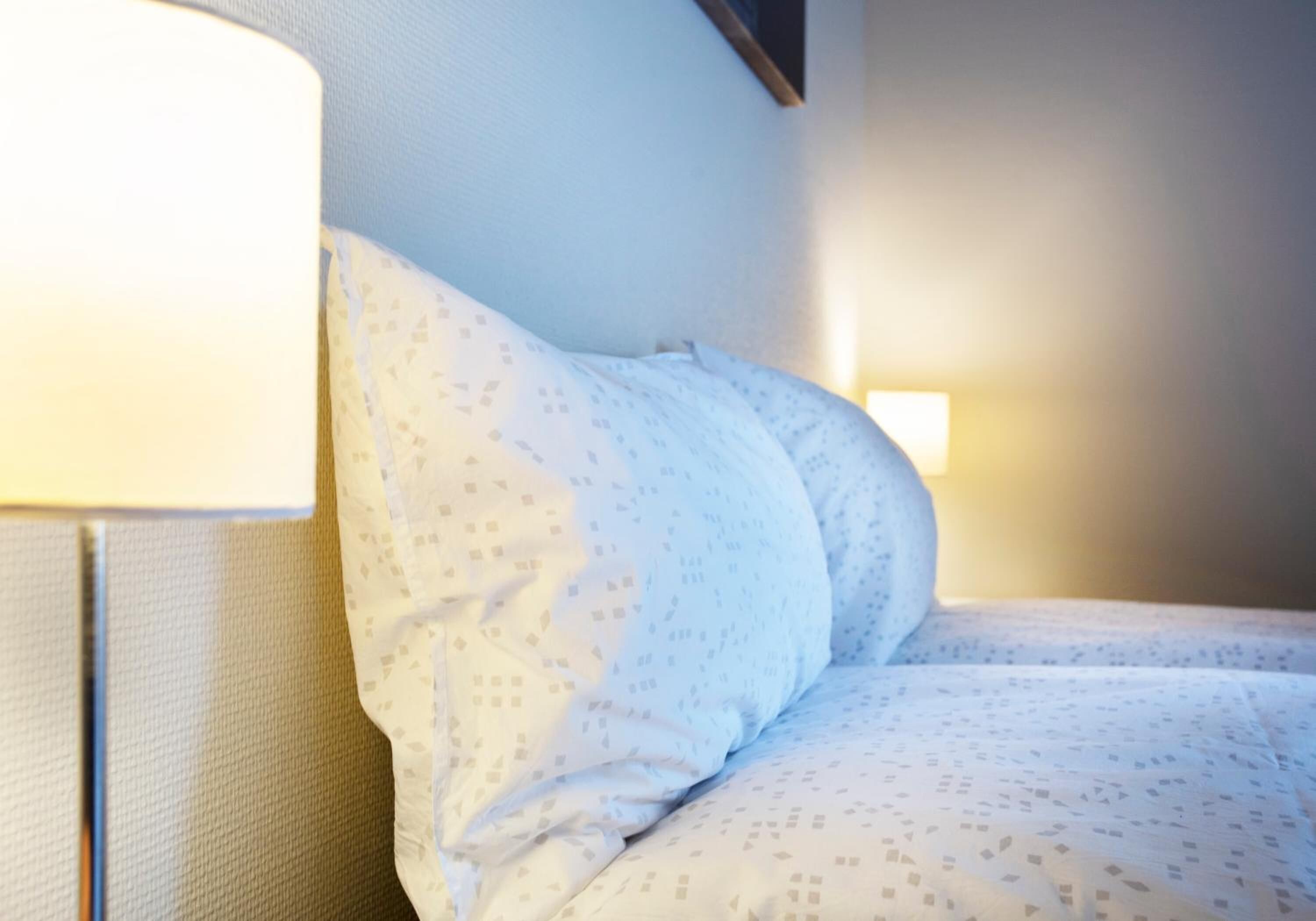 Un lit bien fait, avec une couette à motifs, une lampe de chevet et un luminaire fixé au mur.