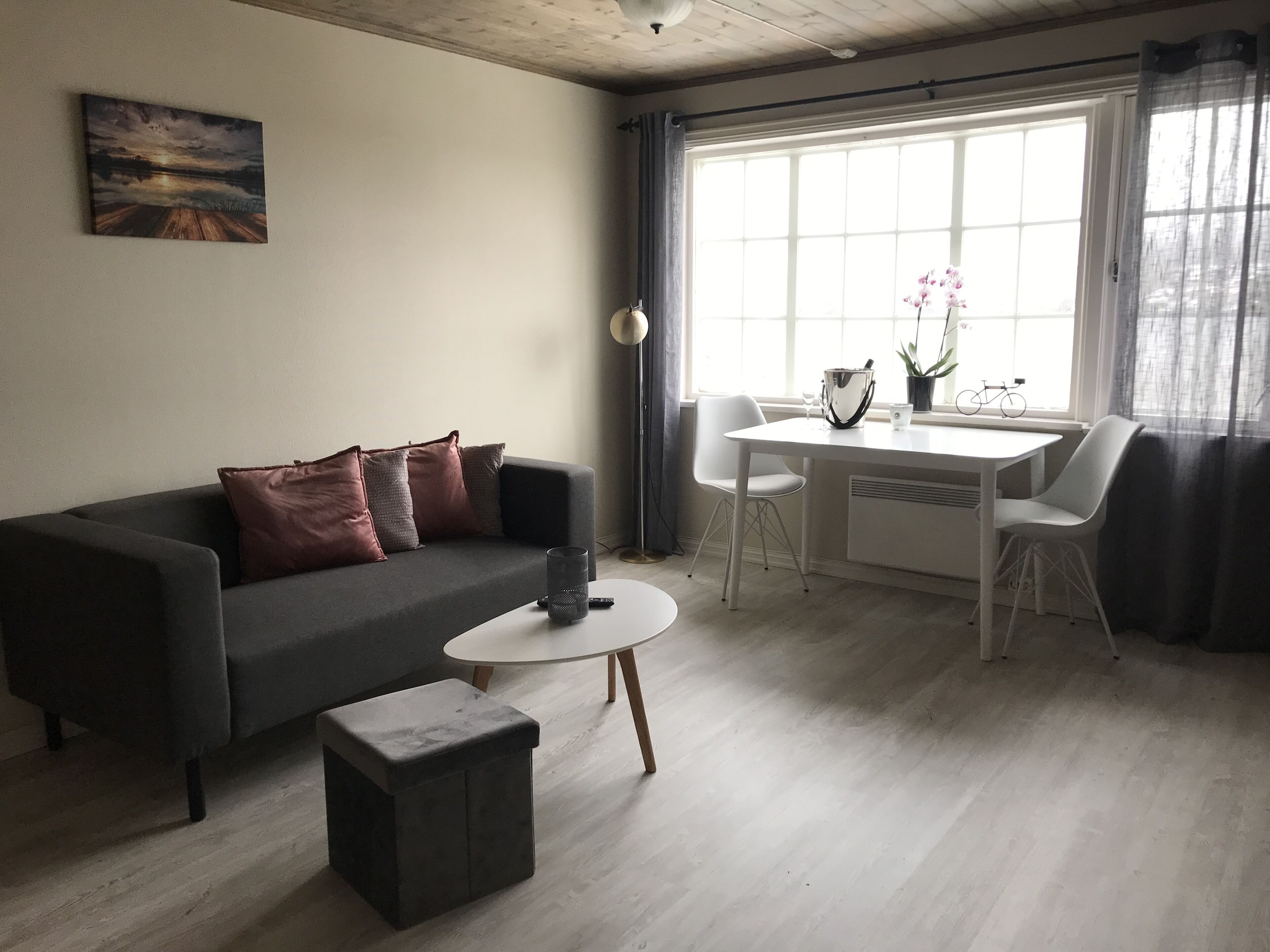 Ett modernt vardagsrum med en grå soffa, ett litet soffbord och en matplats med ett vitt bord och stolar.