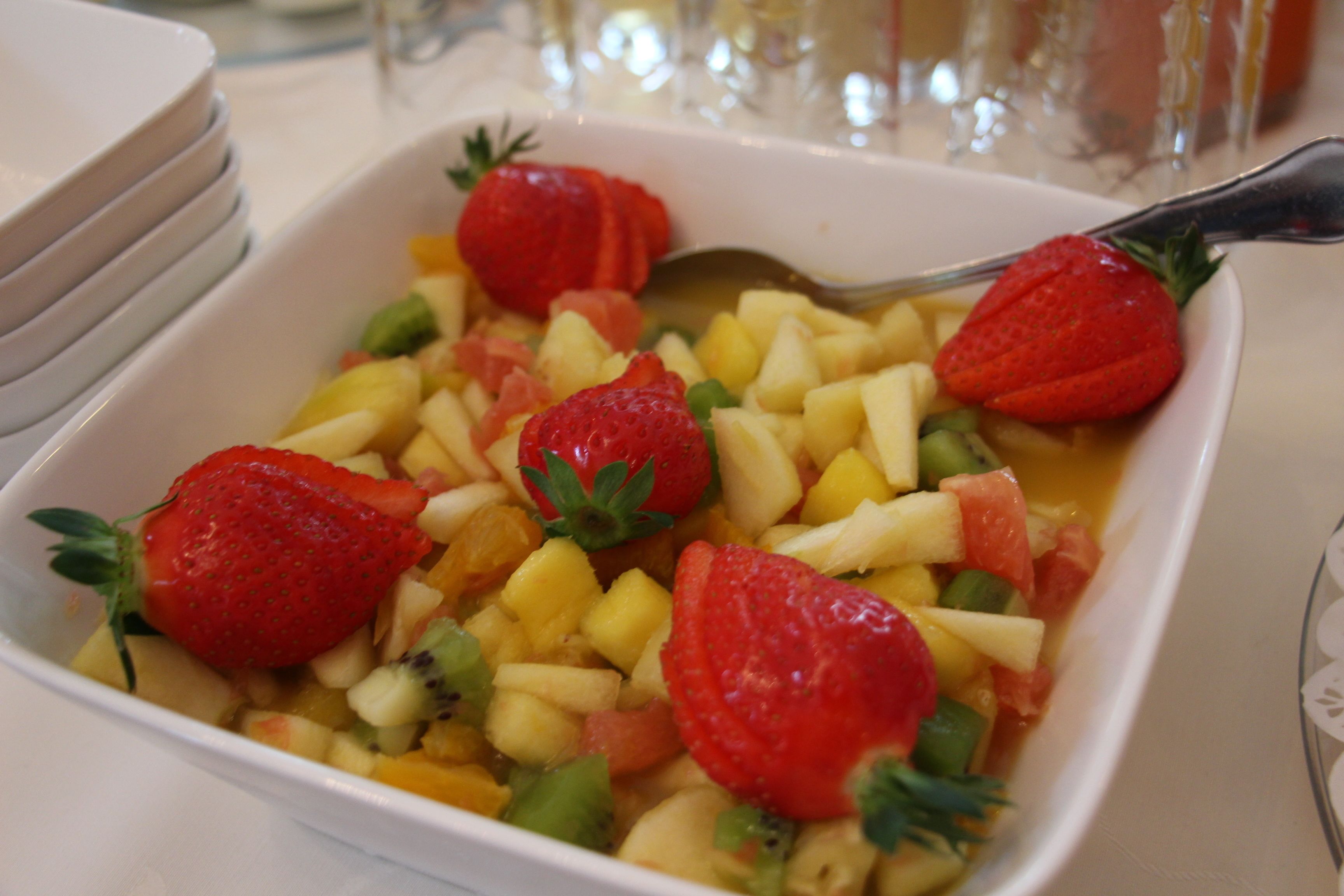 A white square dish with diced fruits and strawberries.