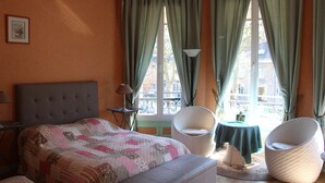 Un dormitorio con una cama, dos sillas, una mesa y un ventanal con cortinas.