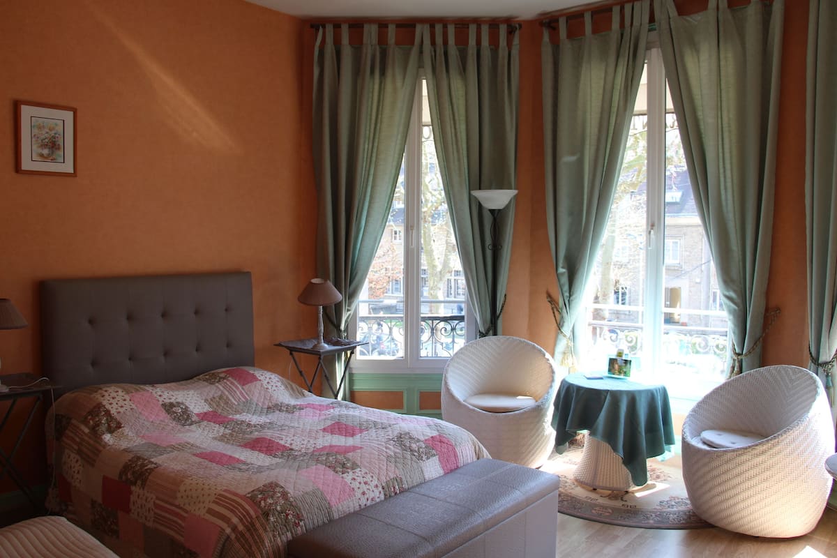 A bedroom with a bed, two chairs, a table, and a window with curtains.