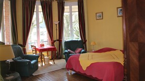 Una habitación con cama, una silla, una mesa y un ventanal con cortinas.
