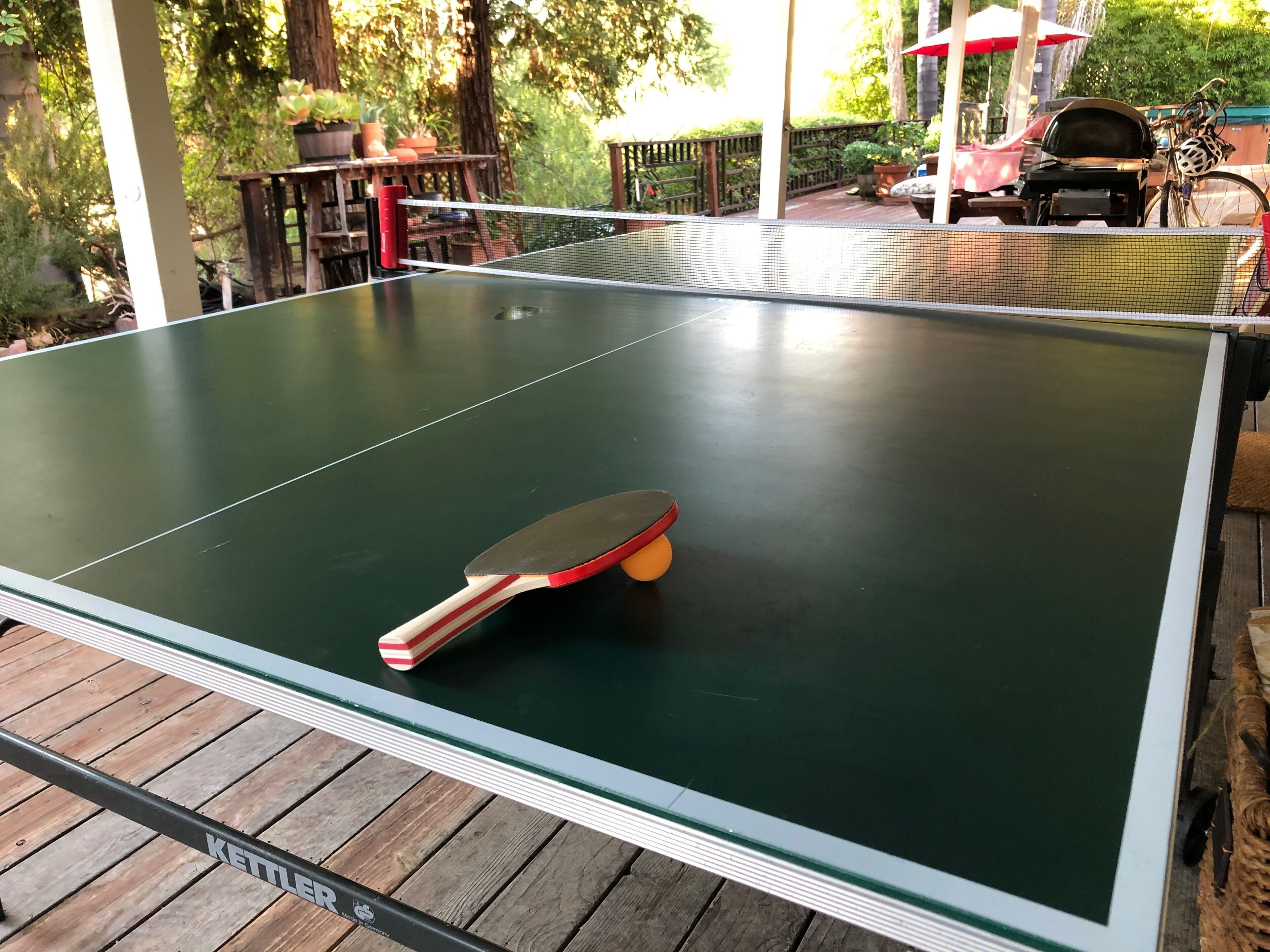 Un tavolo da ping pong con una racchetta, circondato da un pontile in legno.