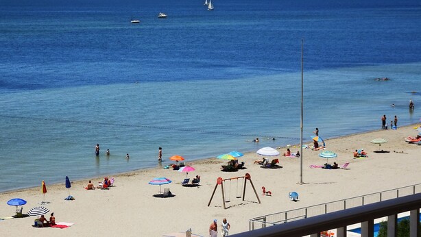 Une plage avec des parasols, des gens et une balançoire.