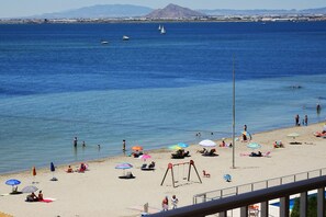 A beach with umbrellas, people, and a swing set.
