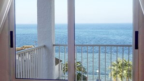 Un balcon avec vue sur la mer, des balustrades blanches et un palmier.