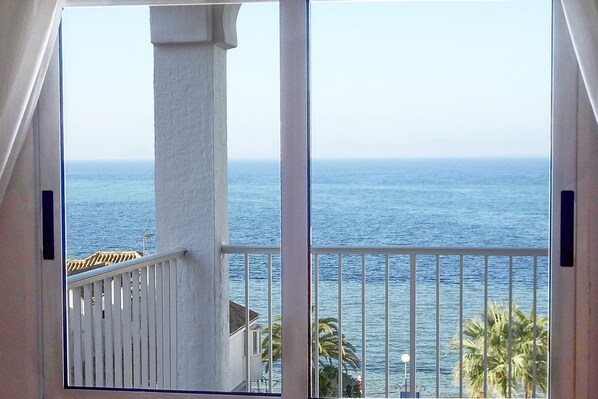 A balcony with a view of the sea, white railings, and a palm tree.