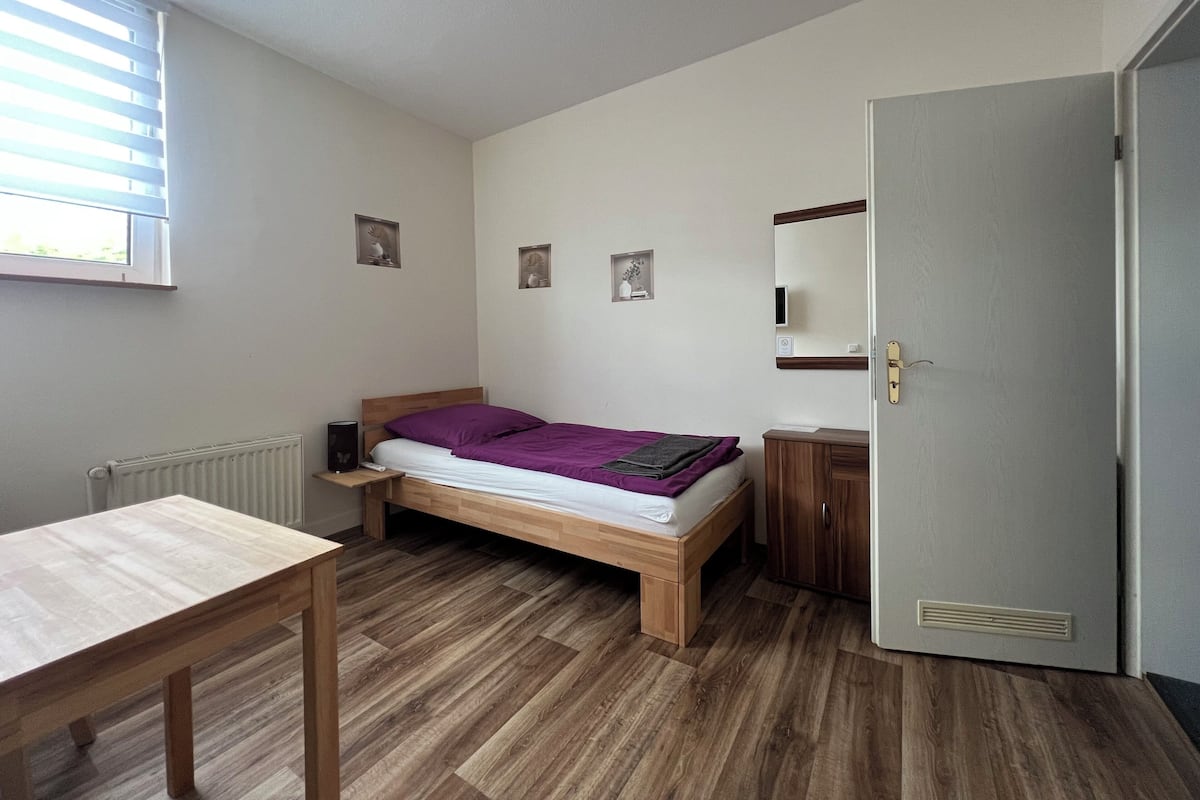 A small, tidy room with a wooden bed, a bedside table, a radiator, and a door.
