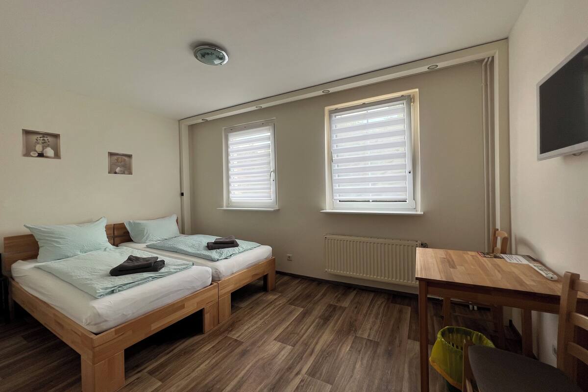 A small, tidy room with two single beds, a wooden desk, a chair, and a radiator.