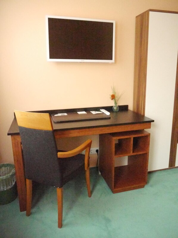 A wooden desk with a chair, a small vase with a plant, and a television mounted on the wall. - Apart Pension Plaue (Brandenburg an der Havel)