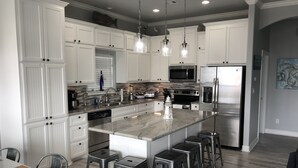 A modern kitchen with white cabinetry, stainless steel appliances, and a central island with bar stools. - Shark Shack ~ 3rd Row Home ~ Holiday Addition ~ Ocean View ~ Basketball Goal (Bolivar Peninsula)