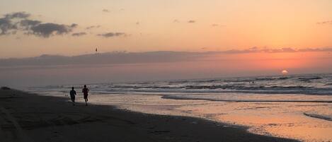 A beach scene with two people walking along the shore during sunset.