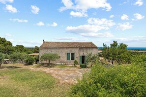 Une maison en pierre avec un toit de tuiles, des volets verts et un petit jardin.