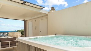A hot tub on a balcony with a view of the sea, a door, and a chair.