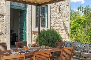 Un espace de restauration en plein air, avec un bâtiment en pierre, une table et des chaises en bois, le tout entouré de verdure.