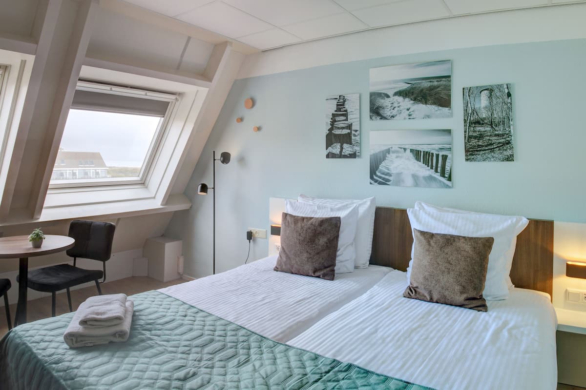 Ein Hotelzimmer mit einem großen Bett, einem Schreibtisch und einem Sessel. An der Wand hängen drei Bilder.