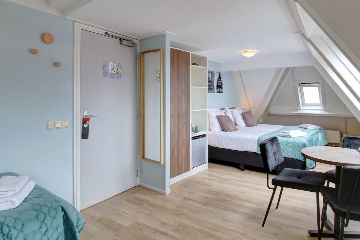 Ein Zimmer mit einem Bett, einem Schreibtisch und einem Stuhl. Es gibt ein Fenster und eine Tür.