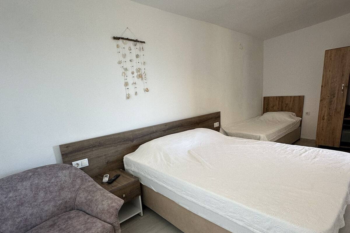 A bedroom with a large bed, a bedside table, a chair, a small table, and a wall-mounted light fixture.