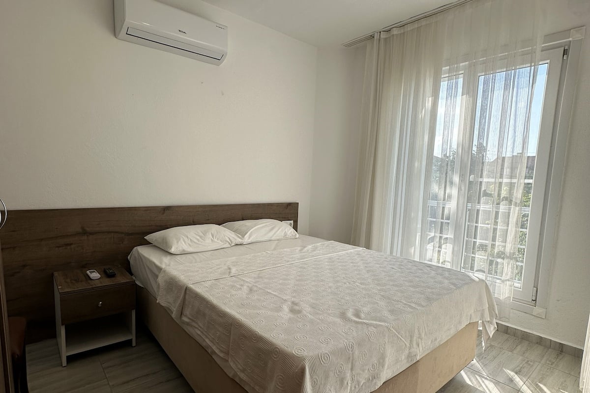 A bedroom with a wooden bed, a nightstand, an air conditioner, and a window with curtains.
