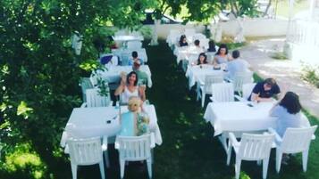 An outdoor seating area with white tables and chairs arranged under trees.