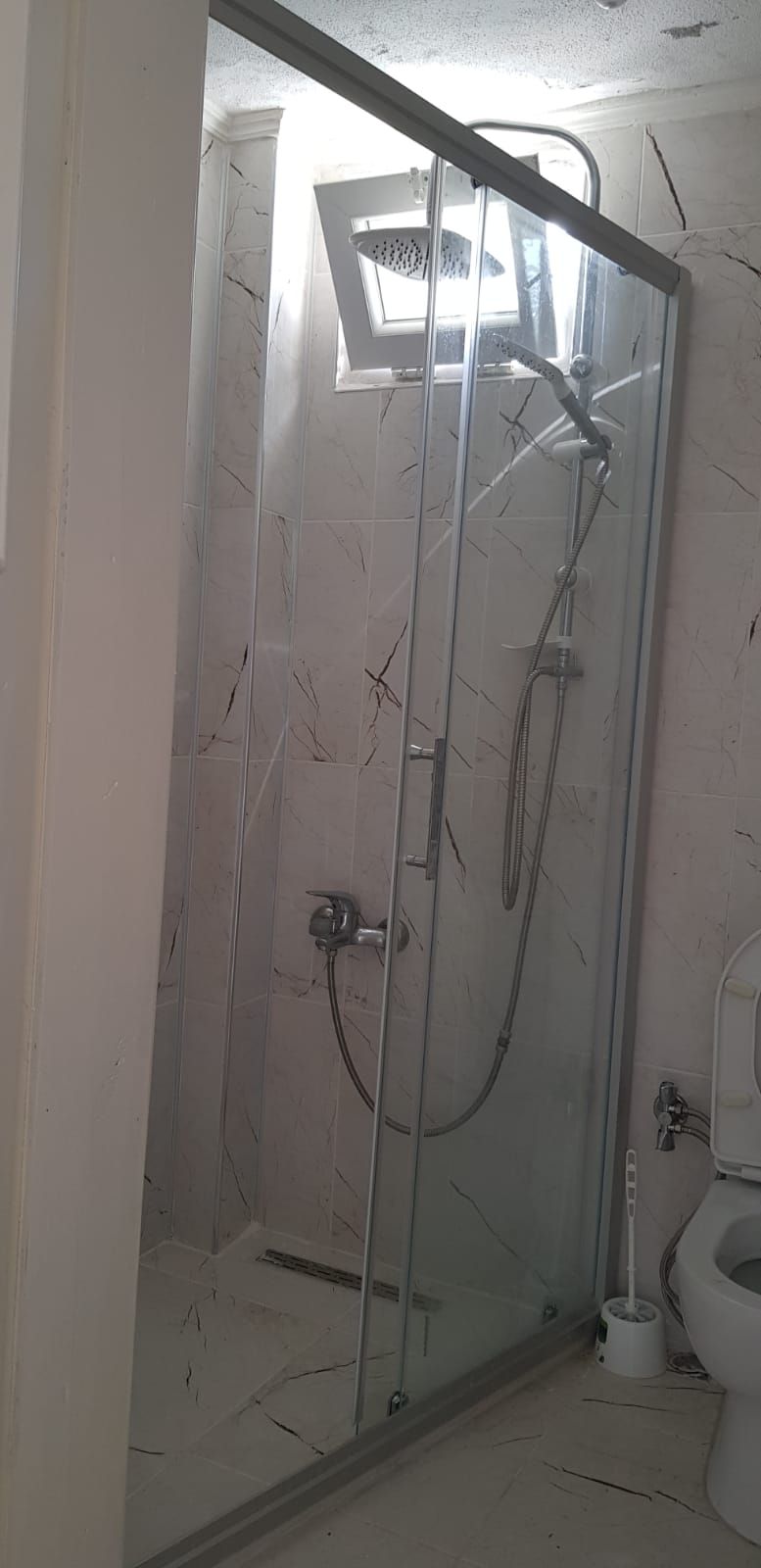 A glass-enclosed shower stall with a handheld showerhead and a handheld faucet.
