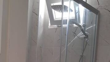 A glass-enclosed shower stall with a handheld showerhead and a handheld faucet.