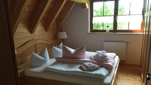Ein Schlafzimmer mit Holzboden, einem Bett mit Kissen und Handtüchern, einem Fenster mit Blick auf Grünflächen und einem Heizkörper.