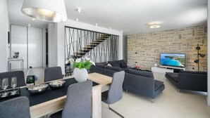 A modern living room with a dining area, a staircase, and a stone wall with a TV.