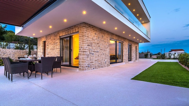 A modern outdoor patio with a stone wall, glass doors, and a dining area with chairs and a table.